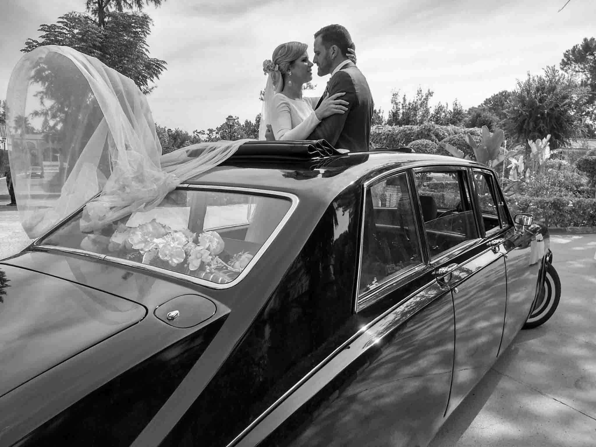 Pareja de novios recién casados sonriendo delante de un coche clásico